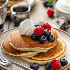 3 pancakes stacked topped with fresh berries and whipped cream