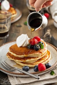 Maple syrup being poured over a stack of fluffy pancakes
