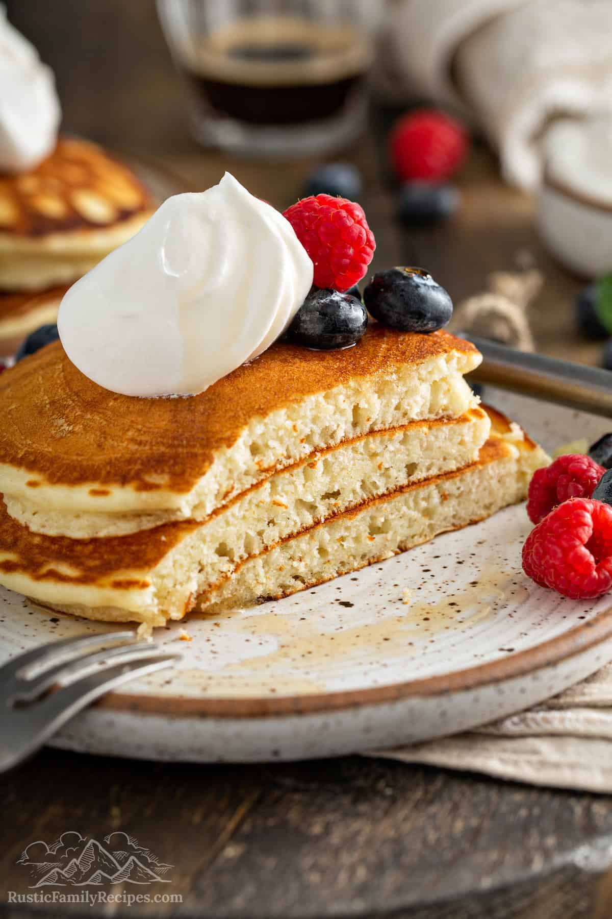A stack of fluffy pancakes on a plate with a bite sliced off