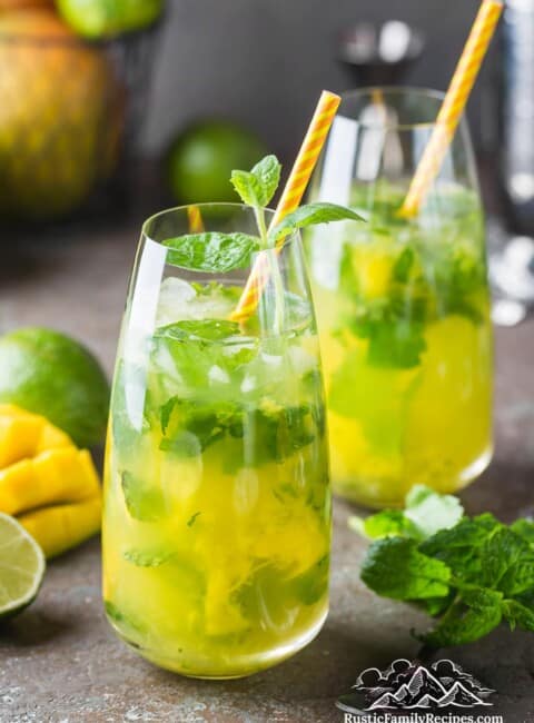 Two mango mojitos in tall glasses with orange straws