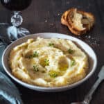 A bowl of homemade mashed potatoes with bread and a glass of wine