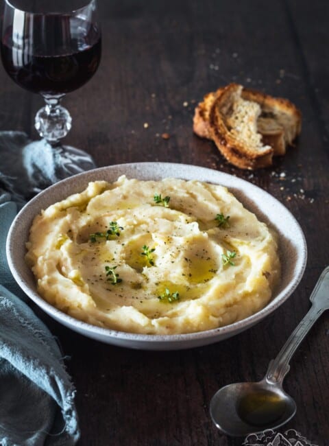 A bowl of homemade mashed potatoes with bread and a glass of wine