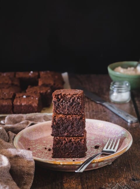 A stack of homemade brownies on a plate with a fork.