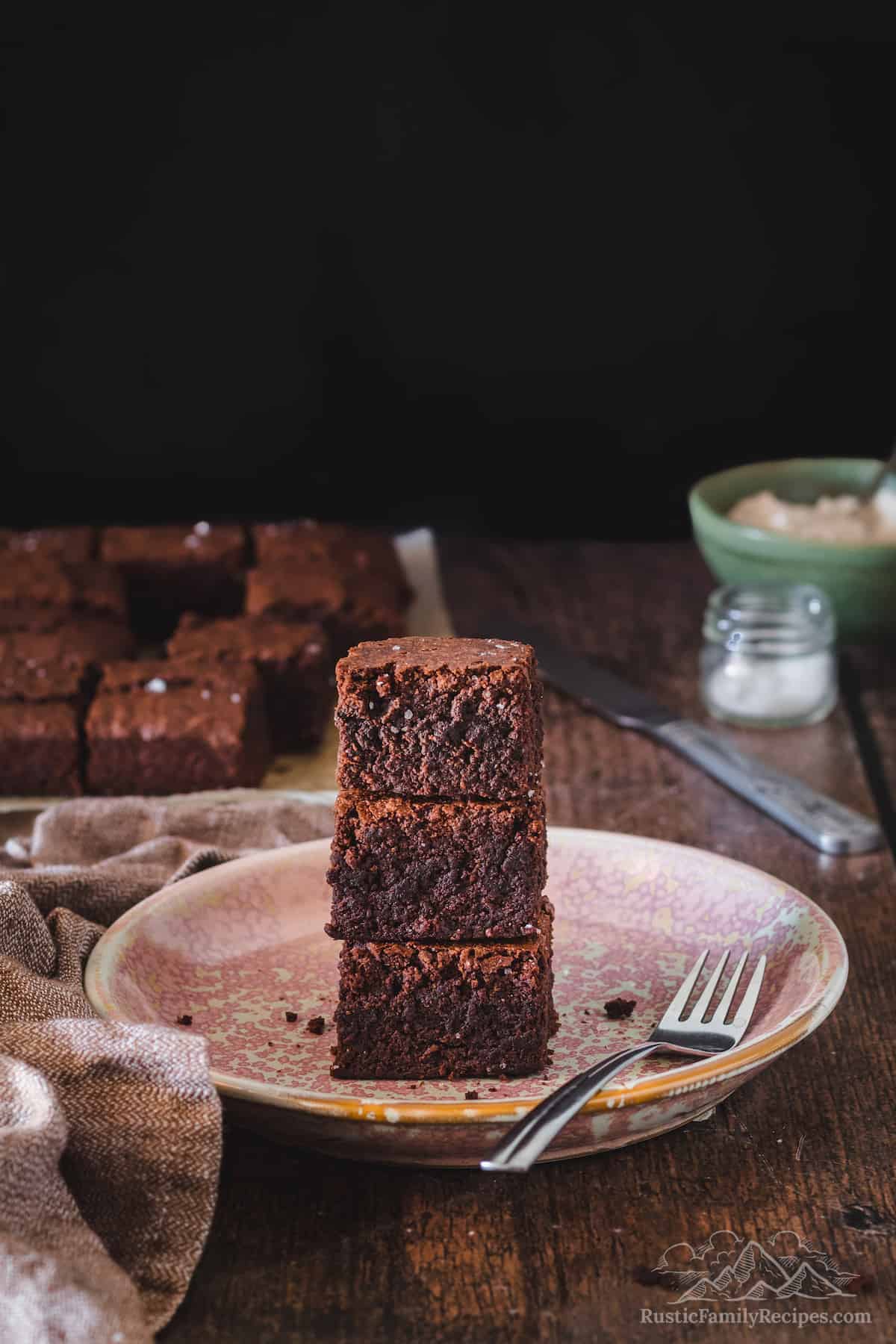A stack of homemade brownies on a plate with a fork.