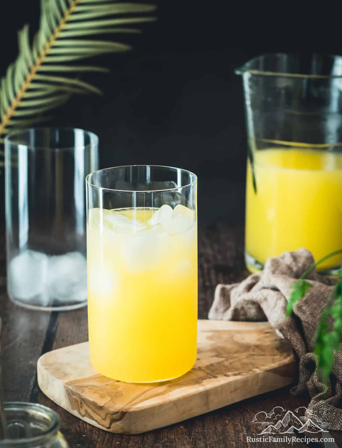 A glass of mango lemonade in front of a pitcher with lemonade