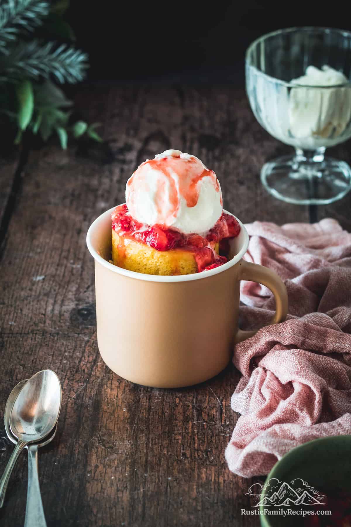 A pink mug on a wood table with vanilla mug cake, topped with ice cream