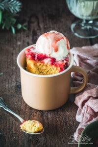 A pink mug on a wood table with vanilla mug cake, strawberries and ice cream