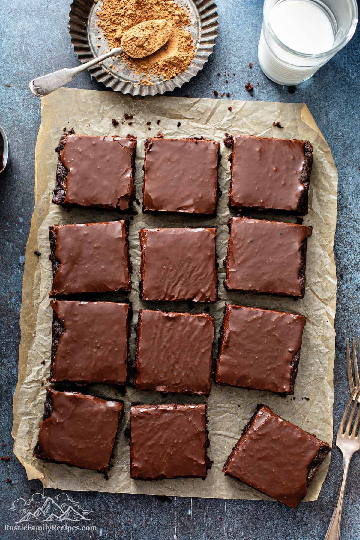 Frosted zucchini brownies on parchment paper with a glass of milk