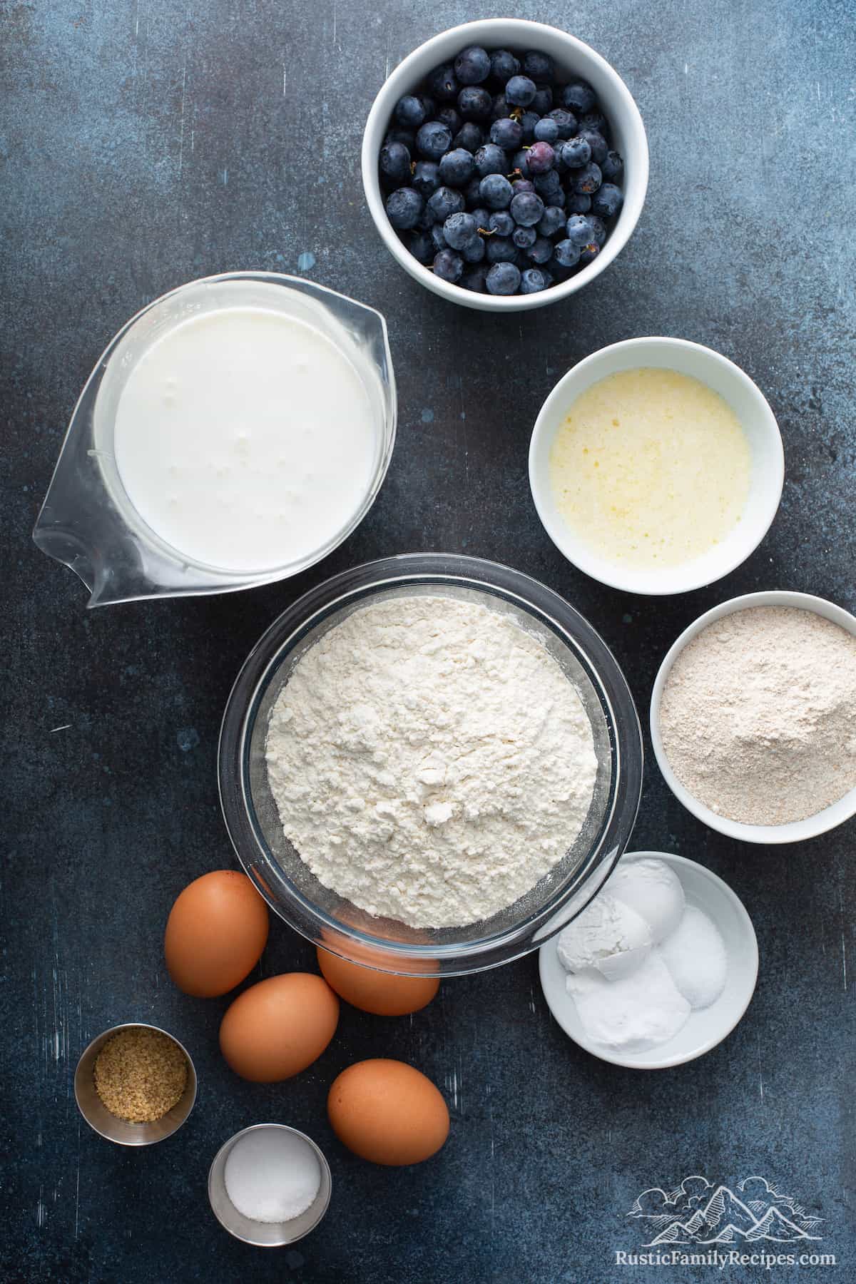 Everything you need for Blueberry Buttermilk Waffles: blueberries, sugar, all purpose and whole wheat flour, baking soda and powder, salt, wheat germ, four eggs, melted butter, and buttermilk.