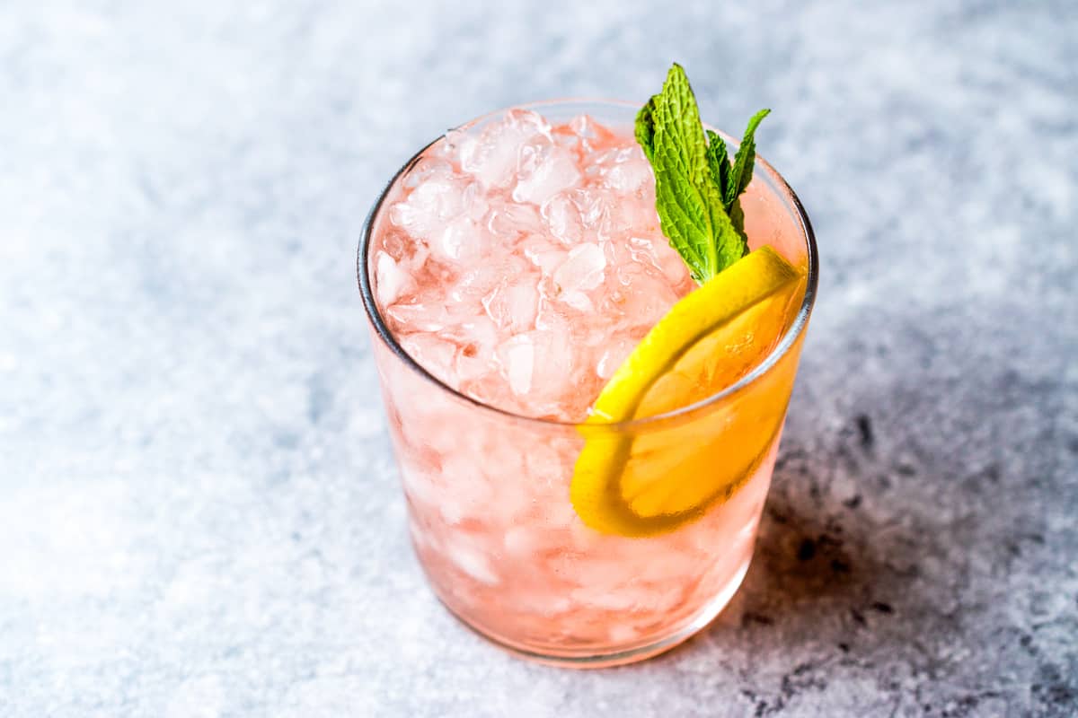 Glass with ice, pink whitney drink, a lemon wedge and mint