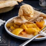 Slice of Peach Mango Pie on white plate, topped with scoop of vanilla ice cream