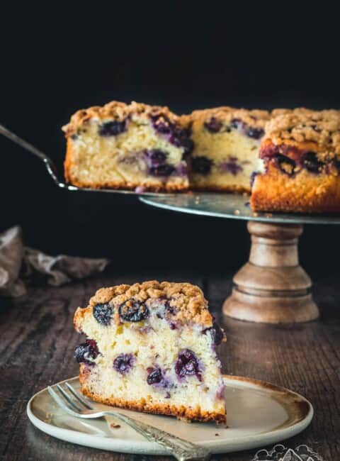 Slice of black currant cake in front of the entire cake on a stand