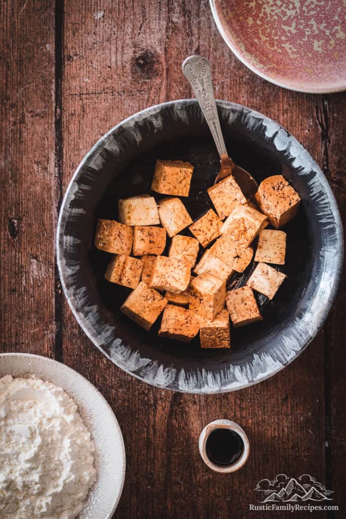 Overhead shot of tofu cubes being tossed with soy sauce