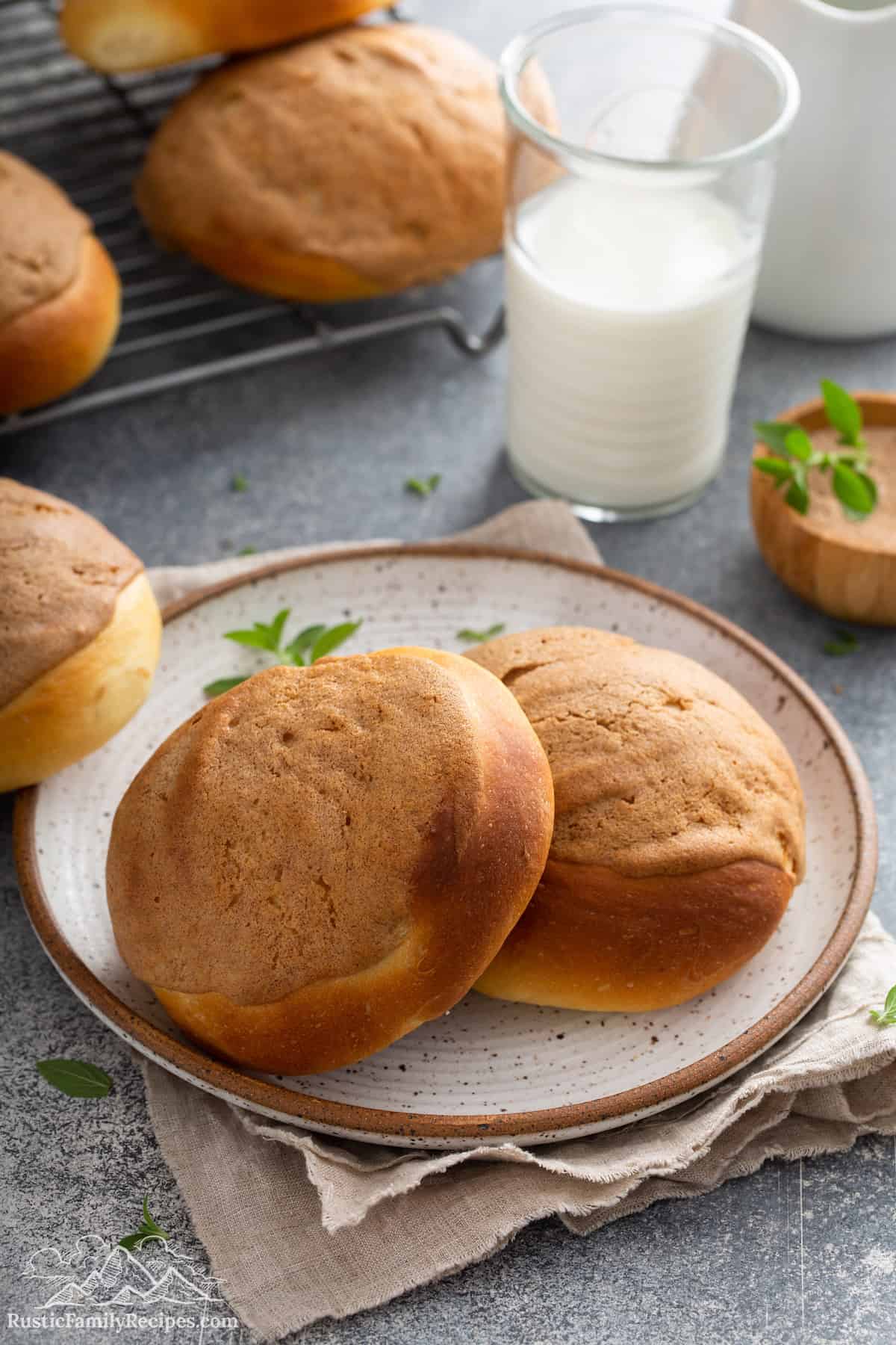 Two Mexican morning buns on a plate, with more buns cooling on rack in background