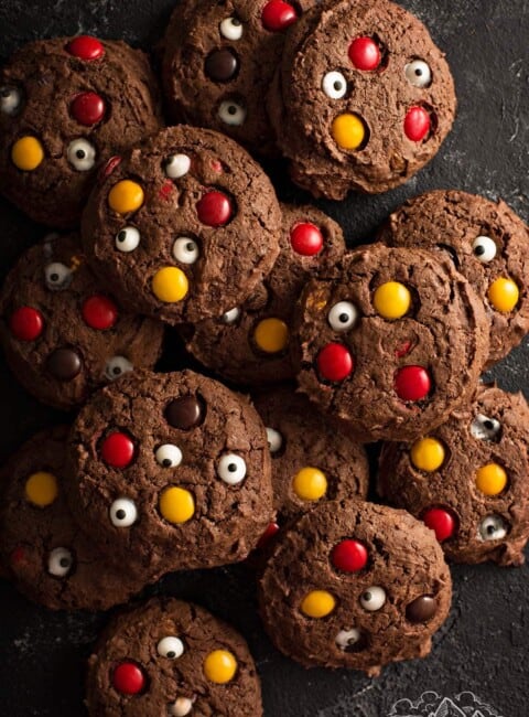 A pile of chocolate cookies with M&M candies and candy eyes.