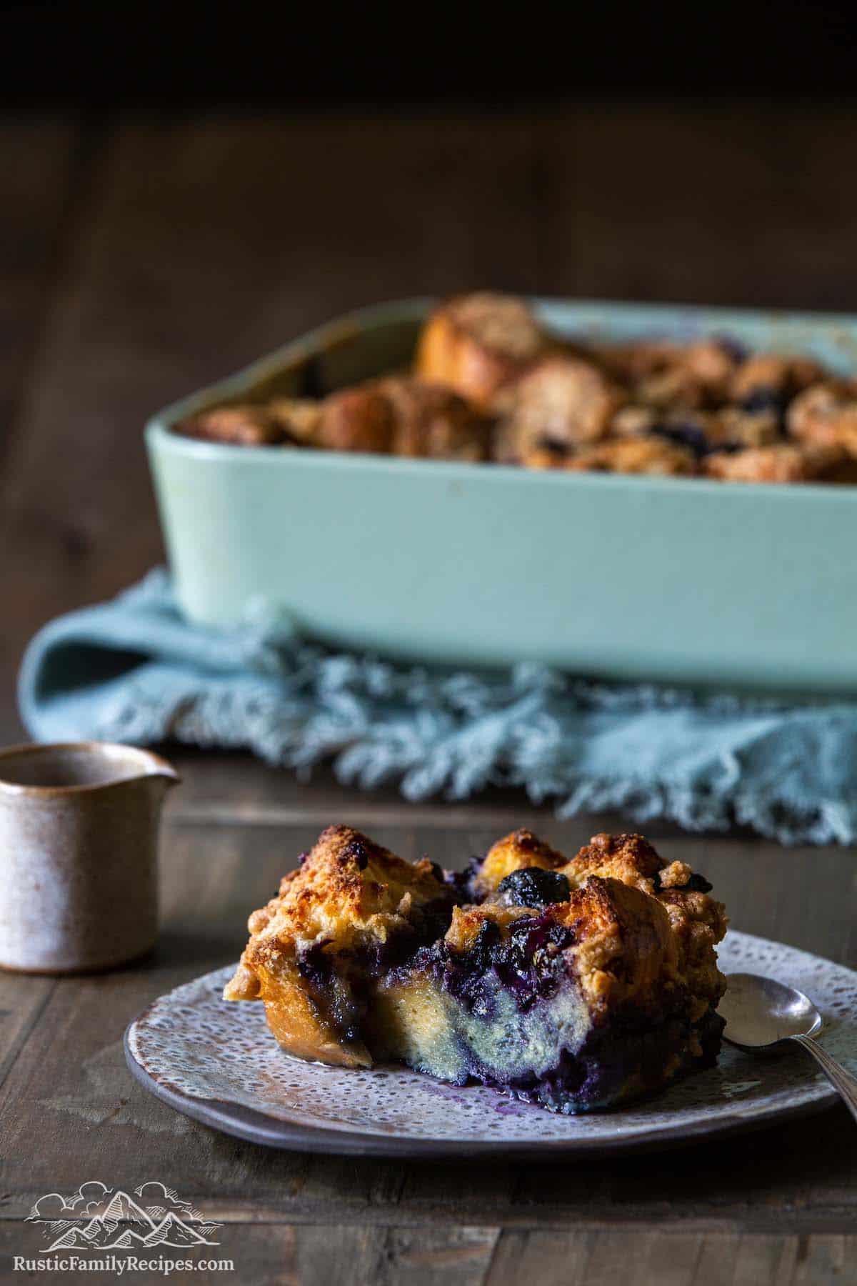 A slice of french toast casserole in front of a blue baking dish