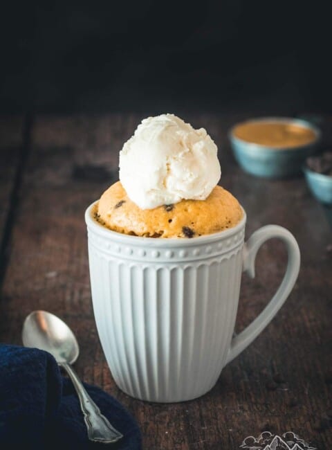 Chocolate chip peanut butter mug cake in a white mug with ice cream and a spoon