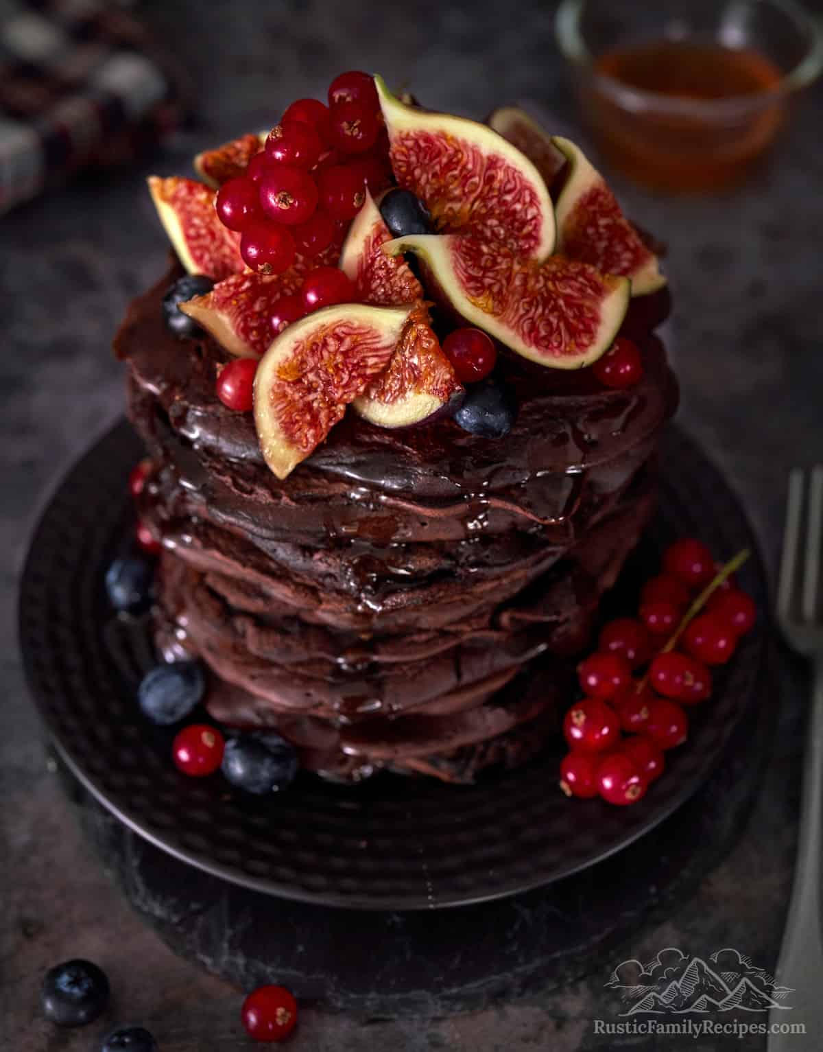 A tall stack of chocolate pancakes topped with figs, currants and blueberries