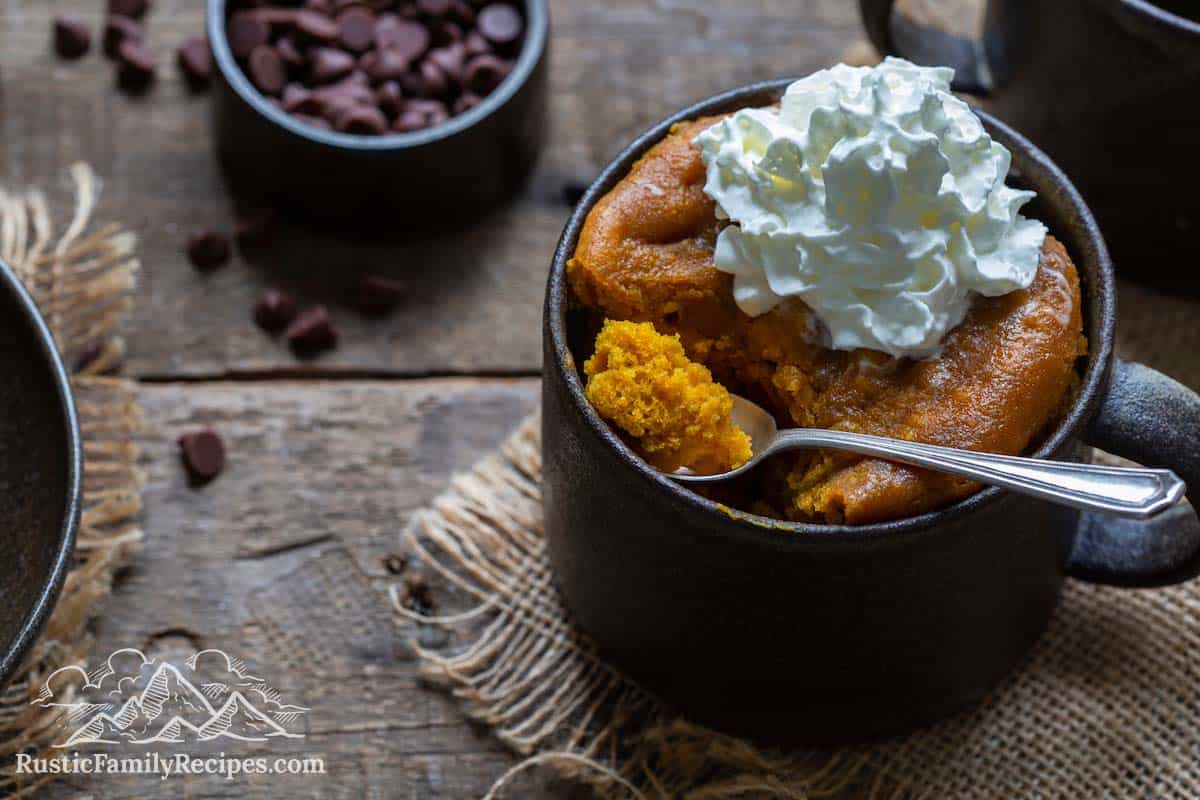 Pumpkin Mug Cake with whipped cream, spoon taking a scoop out