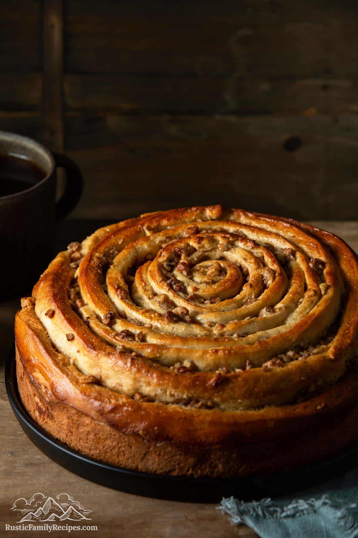 Spiral coffee cake on rustic wooden table with coffee mug in background