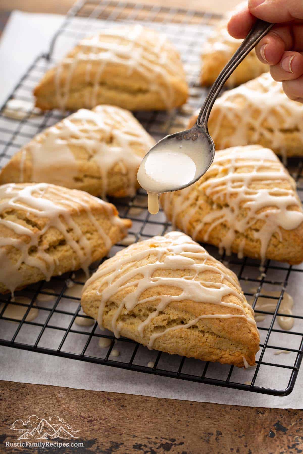 Spooning maple glaze over freshly baked scones on wire cooling rack