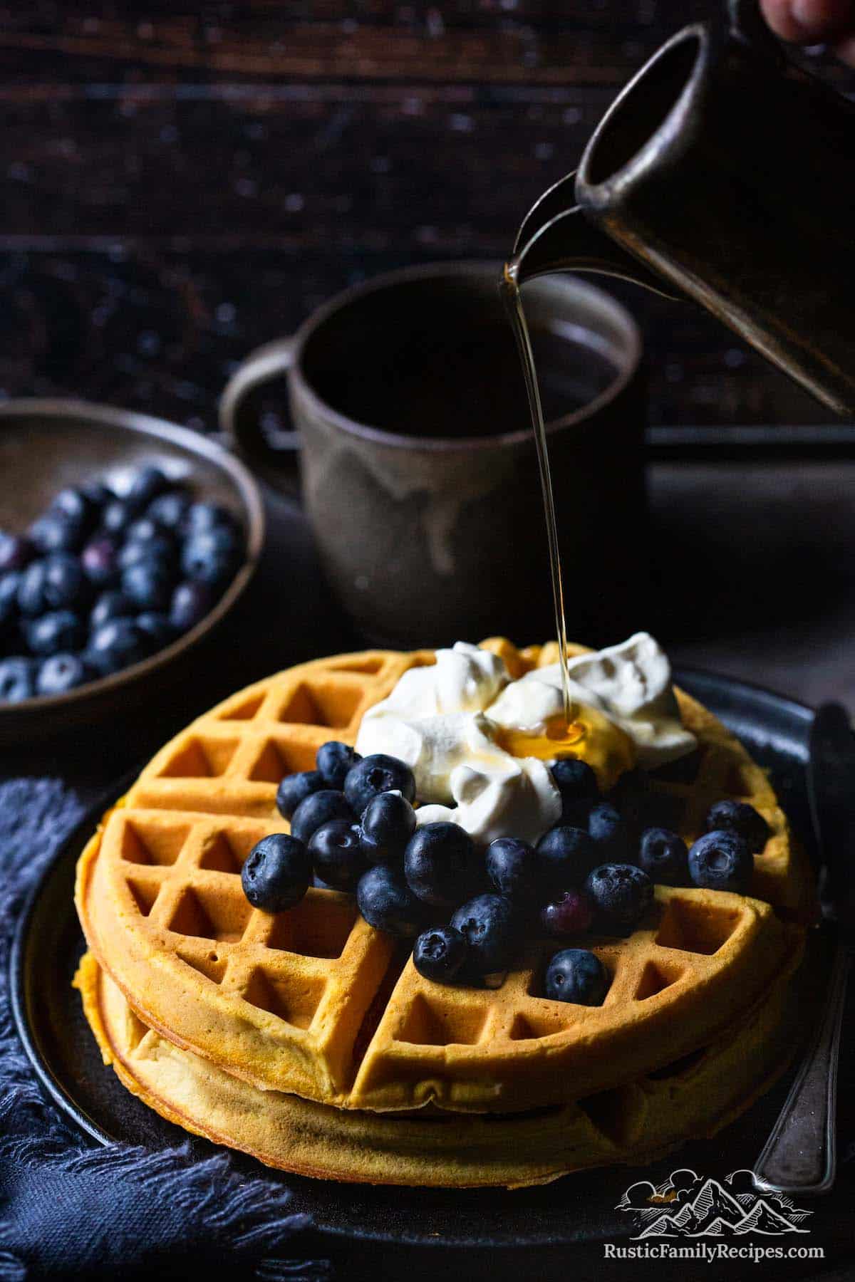 Stack of pumpkin waffles topped with blueberries, whipped cream and syrup