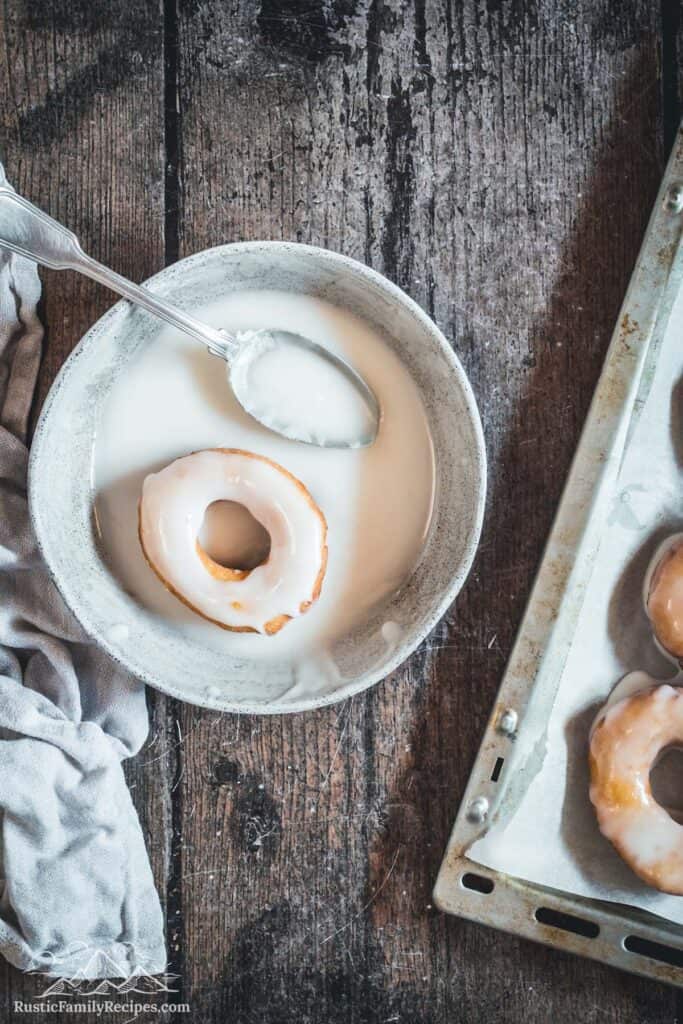 Sour cream donut in bowl of glaze with spoon