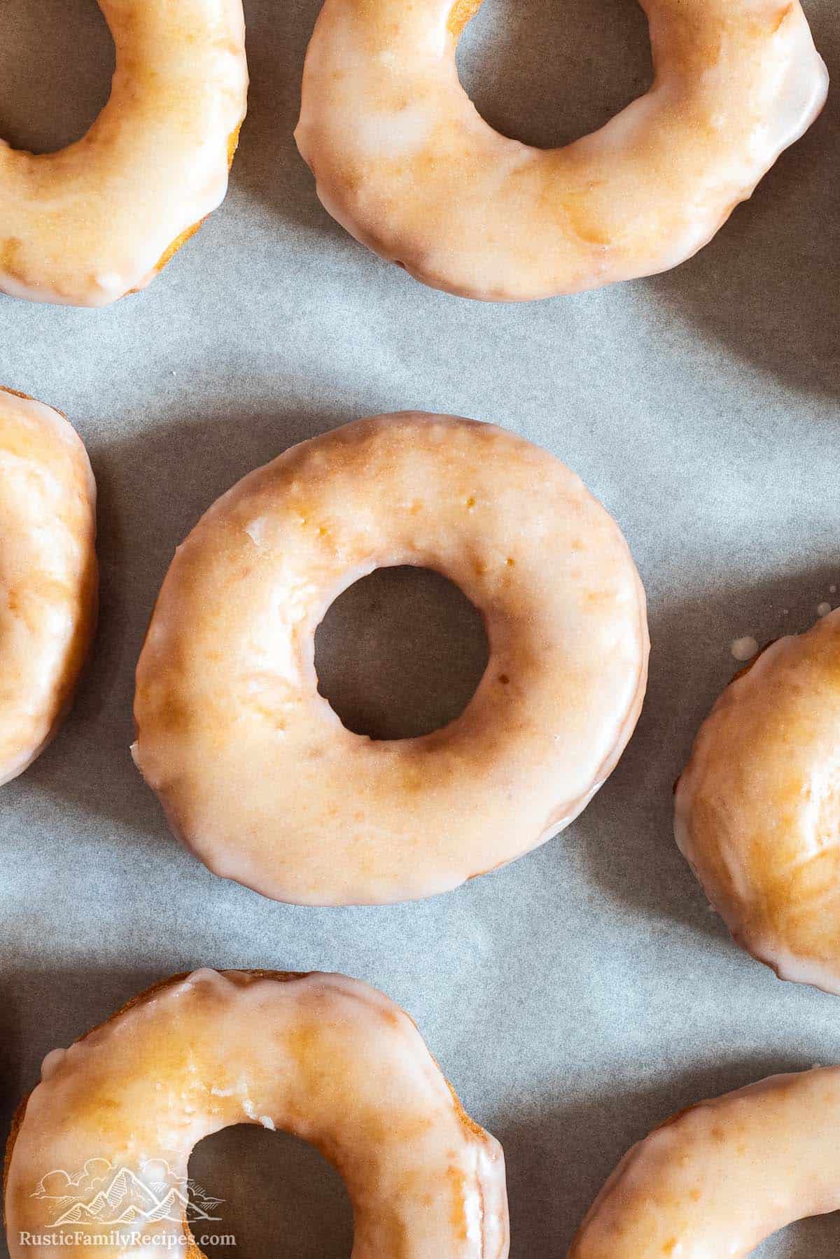 Overhead view of glazed donuts on parchment lined baking sheet