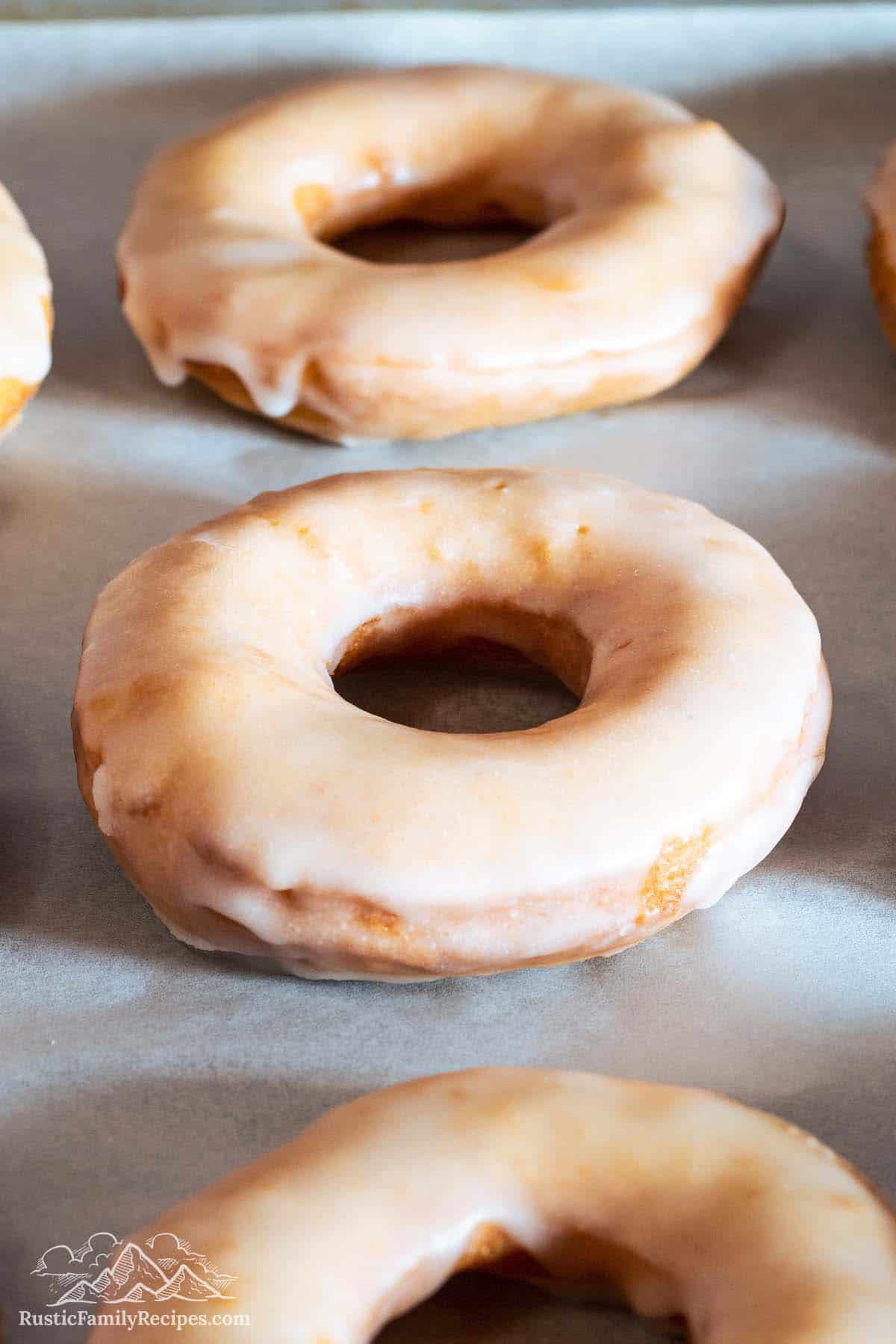 Three glazed donuts on parchment lined baking sheet