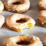 Sour cream donuts on parchment lined baking sheet with bite taken out of one