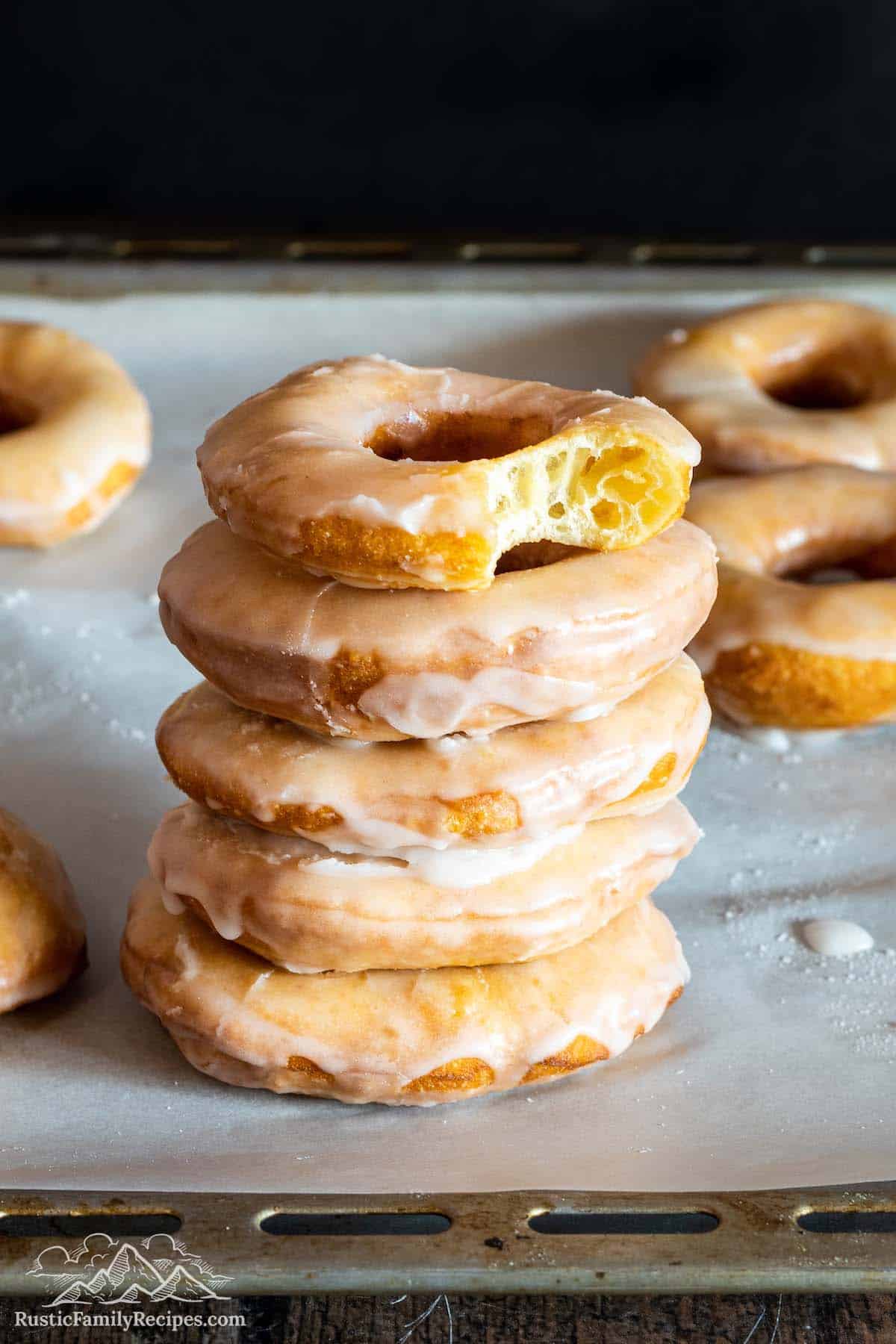 Stack of glazed sour cream donuts with bite taken out of top one