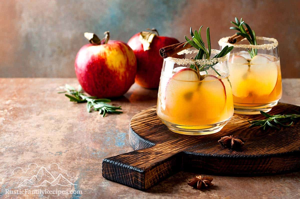 Two apple cider margaritas on a wood cutting board with apples
