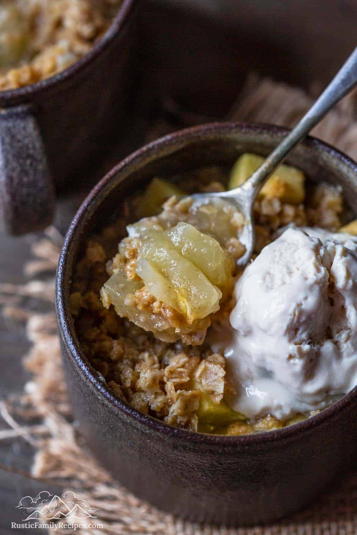 Apple crumble in a mug with ice cream and a spoon scooping some out