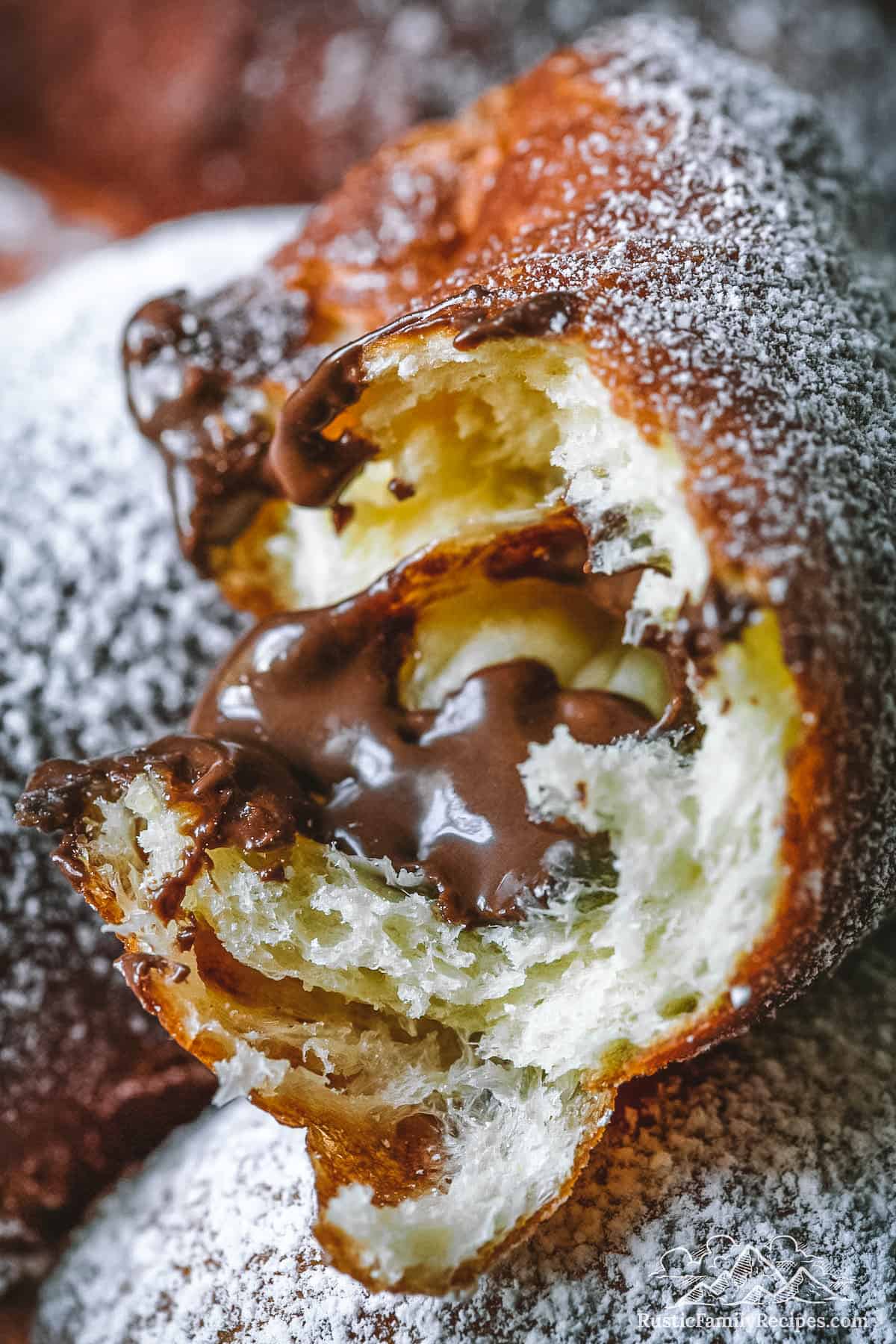 Close up of a beignet with a bite taken out and nutella oozing out