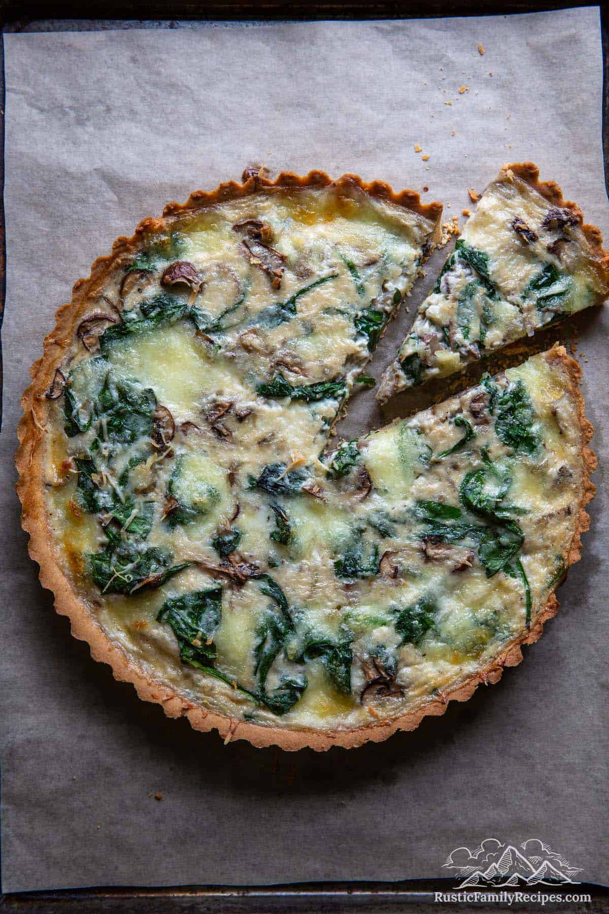 Spinach mushroom quiche on parchment paper with a slice taken out