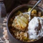 Apple crisp in a mug, a spoon taking a scoop out with ice cream on the side