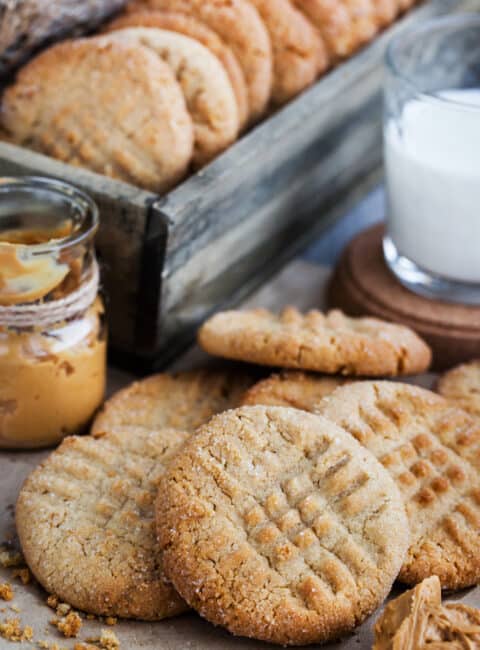 A pile of peanut butter cookies next to a glass of milk