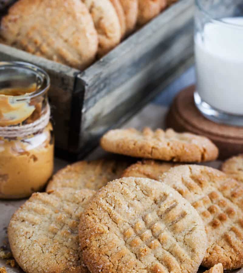 A pile of peanut butter cookies next to a glass of milk