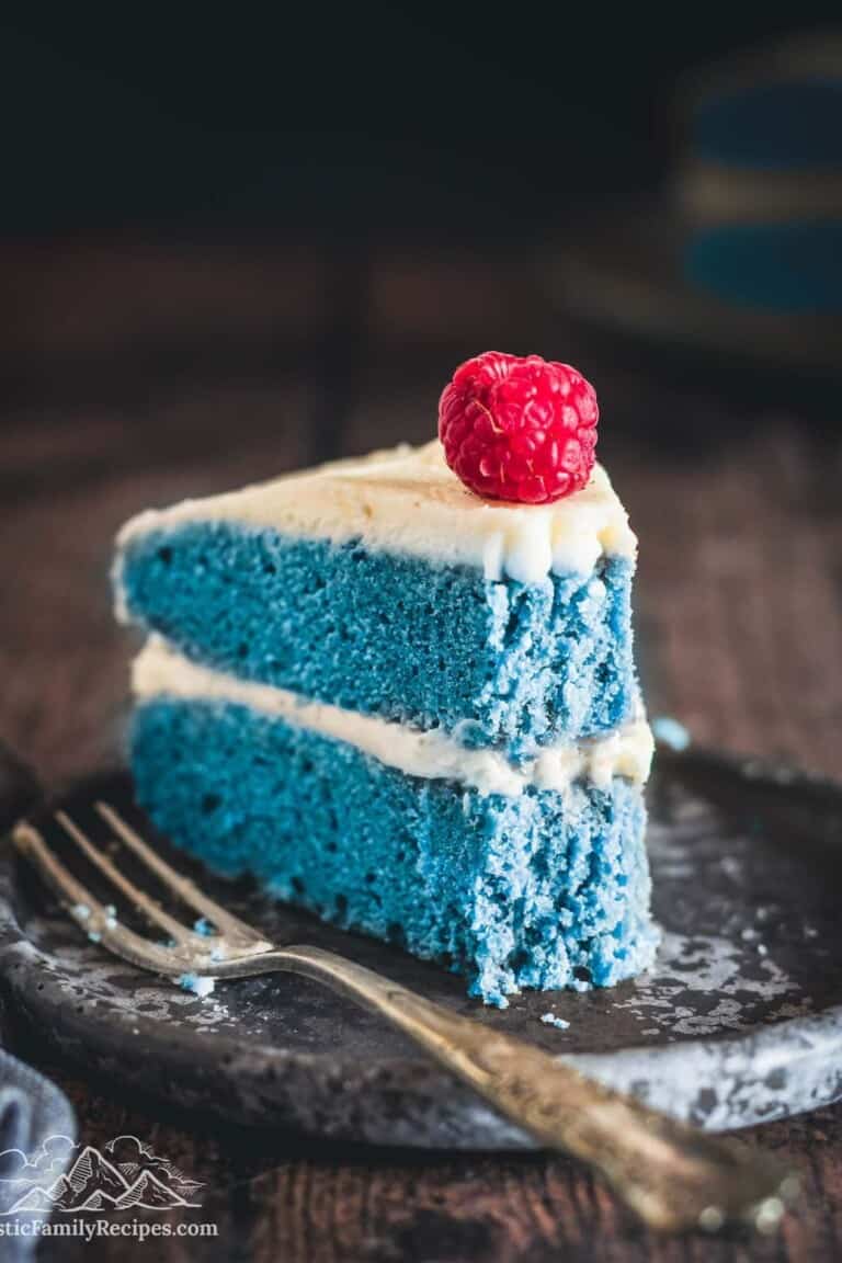 A slice of blue cake with a bite taken out, a raspberry on top of the slice