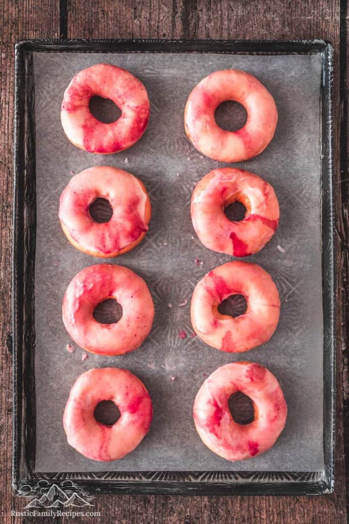 Pink glazed homemade donuts on a baking sheet