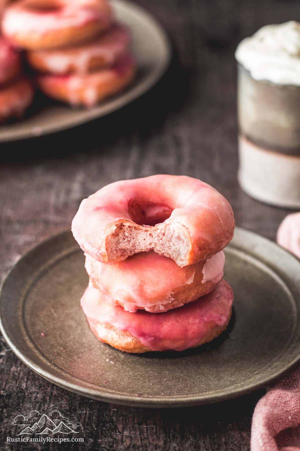 3 pink donuts stacked on a plate with a bite taken out of the top one