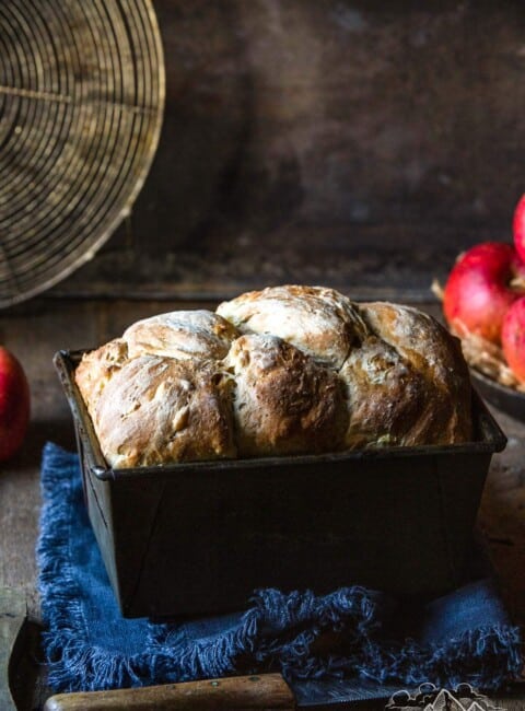 A loaf of apple bread in a baking tin next to an apple