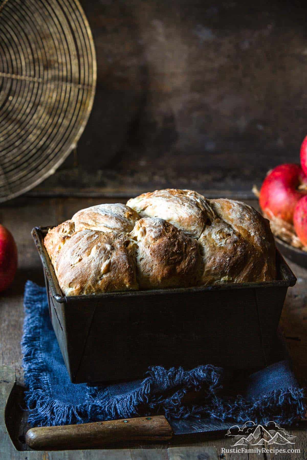 A loaf of apple bread in a baking tin next to an apple