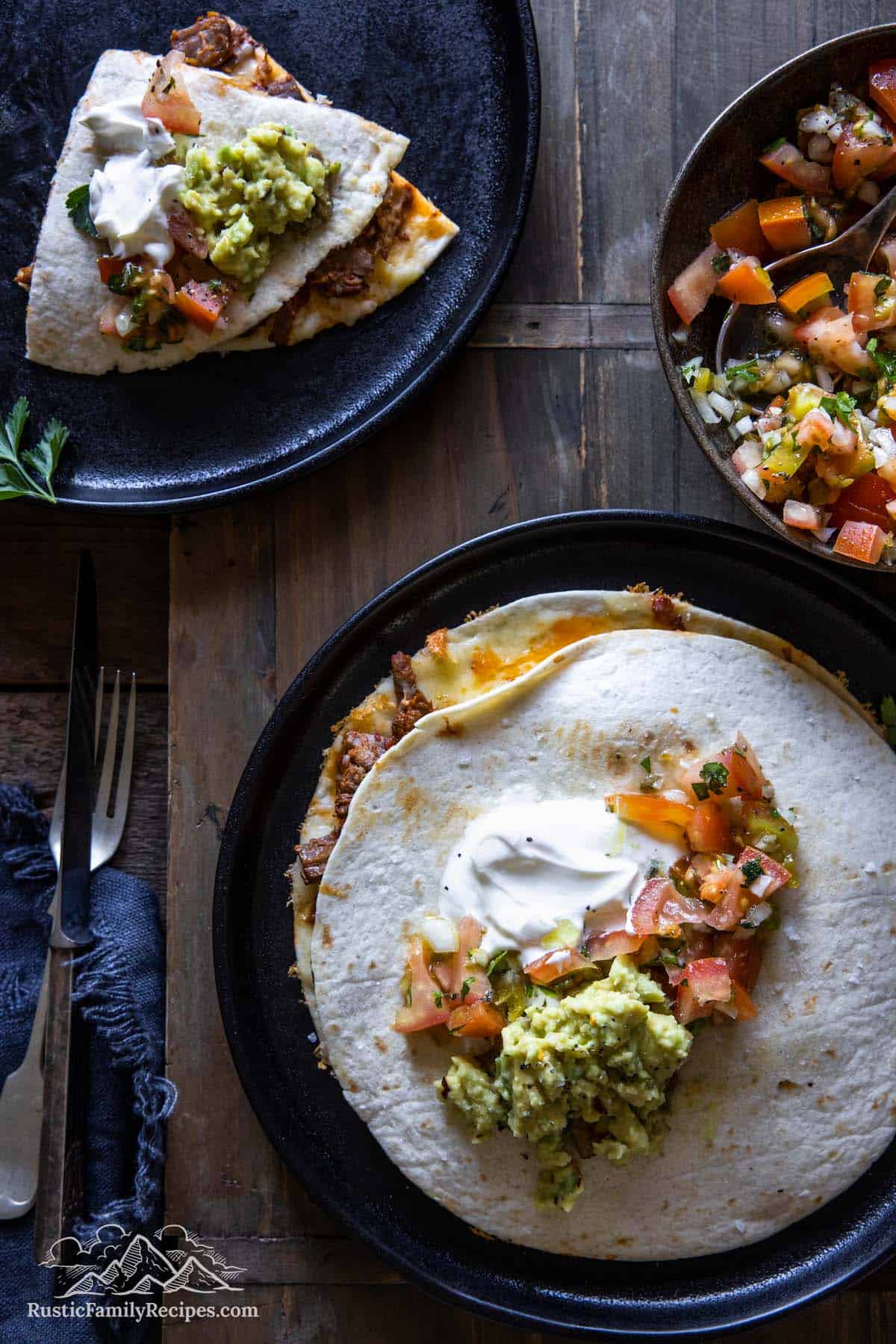 Uncut quesadilla on a plate, next to a bowl of salsa and a plate with quesadilla wedges