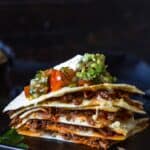 Stack of quesadilla wedges where you can see the birria meat, topped with fixings