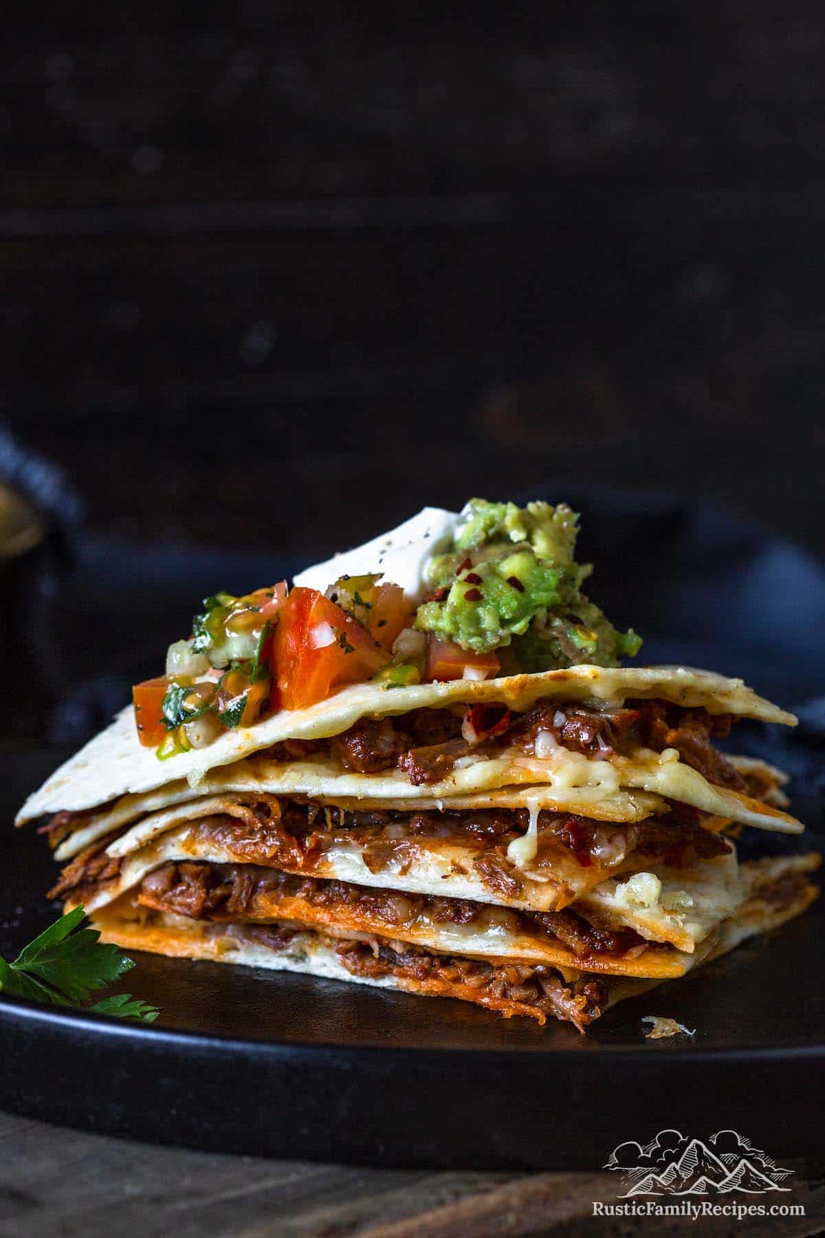 Stack of quesadilla wedges where you can see the birria meat, topped with salsa, guacamole and sour cream.