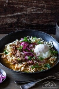 A grey bowl filled with birria ramen noodles topped with an egg