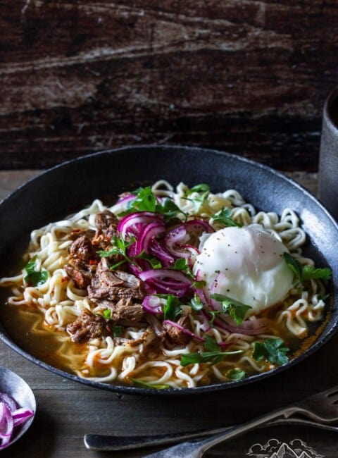 A grey bowl filled with birria ramen noodles topped with an egg