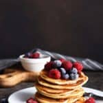 A tall stack of pancakes topped with berries and syrup