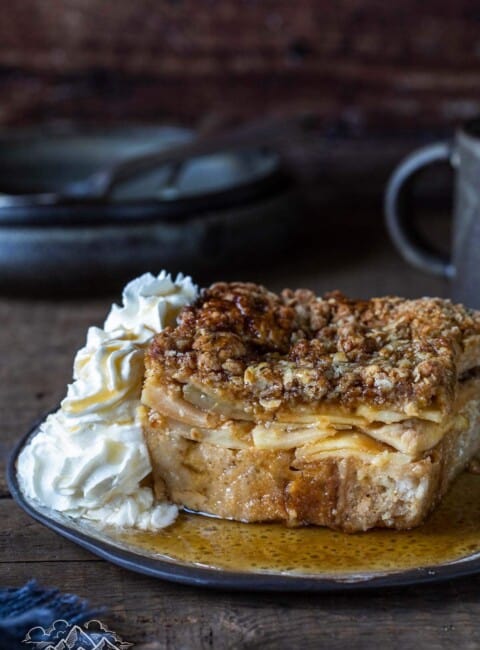 A slice of baked french toast apple casserole on a plate with whipped cream